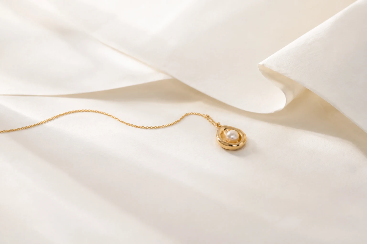Gold pearl pendant and chain across sculpted ivory paper